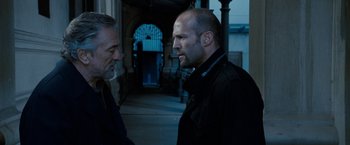 Movie still from “Killer Elite” (2011), directed by Gary McKendry – Two men are talking in a dark alley; Close Up shot, Over the shoulder angle