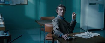 Movie still from “Killer Elite” (2011), directed by Gary McKendry – A man sitting at a table in front of a cell phone; Medium shot, Over the shoulder angle