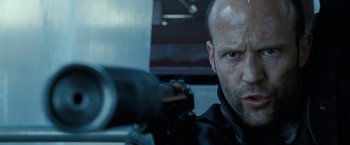 Movie still from “Killer Elite” (2011), directed by Gary McKendry – A man with a gun in his hand and wearing a black jacket; Close Up shot, Low angle