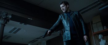 Movie still from “Killer Elite” (2011), directed by Gary McKendry – A man in a leather jacket holding a gun in a room; Medium shot, Low angle