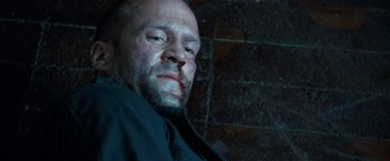 Movie still from “Killer Elite” (2011), directed by Gary McKendry – A person wearing a black shirt; Close Up shot, Low angle