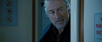 Movie still from “Killer Elite” (2011), directed by Gary McKendry – A man with grey hair and a goatee looking at the camera; Close Up shot, Over the shoulder angle