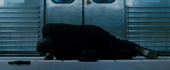 Movie still from “Killer Elite” (2011), directed by Gary McKendry – A person laying on the ground in front of a train; Wide shot, Overhead angle