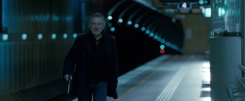 Movie still from “Killer Elite” (2011), directed by Gary McKendry – A man walking down a train platform at night; Medium shot, Over the shoulder angle