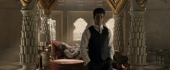 Movie still from “Killer Elite” (2011), directed by Gary McKendry – A man in a suit and tie standing next to a chair; Medium shot, Low angle