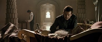 Movie still from “Killer Elite” (2011), directed by Gary McKendry – A man sitting at a table in front of a woman; Medium shot, Over the shoulder angle