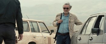 Movie still from “Killer Elite” (2011), directed by Gary McKendry – An older man standing next to an old car; Medium shot, Over the shoulder angle