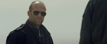 Movie still from “Killer Elite” (2011), directed by Gary McKendry – A bald man wearing sunglasses and a black jacket; Close Up shot, Low angle