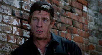 Movie still from “Killer Joe” (2011), directed by William Friedkin – A person wearing a hat near a brick wall; Close Up shot, Over the shoulder angle
