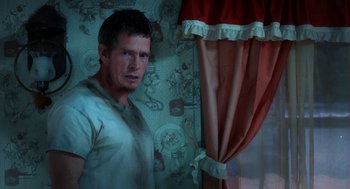 Movie still from “Killer Joe” (2011), directed by William Friedkin – A man standing in front of a window with curtains; Medium shot, Over the shoulder angle