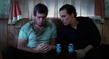 Movie still from “Killer Joe” (2011), directed by William Friedkin – A couple of men sitting next to each other on top of a table; Medium shot, Over the shoulder angle