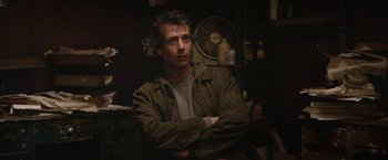 Movie still from “Killing Them Softly” (2012), directed by Andrew Dominik – A man with his arms crossed sitting in a room; Medium shot, Over the shoulder angle