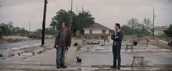 Movie still from “Killing Them Softly” (2012), directed by Andrew Dominik – Two men and a dog standing in a flooded area; Wide shot, Over the shoulder angle