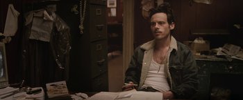 Movie still from “Killing Them Softly” (2012), directed by Andrew Dominik – A man sitting at a table with papers in front of him; Medium shot, Over the shoulder angle