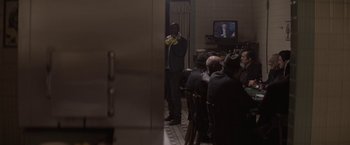 Movie still from “Killing Them Softly” (2012), directed by Andrew Dominik – A group of people sitting in a room watching a tv; Medium shot, Over the shoulder angle