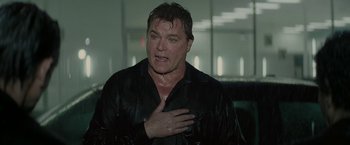 Movie still from “Killing Them Softly” (2012), directed by Andrew Dominik – A man in a black shirt is holding his hand over his heart; Medium shot, Low angle