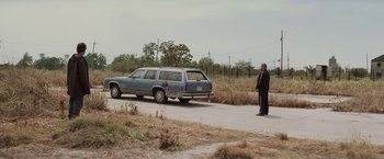 Movie still from “Killing Them Softly” (2012), directed by Andrew Dominik – A man standing next to an old car on the side of the road; Wide shot, Over the shoulder angle