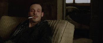 Movie still from “Killing Them Softly” (2012), directed by Andrew Dominik – A man sitting on top of a couch with a cigarette in his mouth; Close Up shot, Low angle
