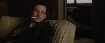 Movie still from “Killing Them Softly” (2012), directed by Andrew Dominik – A man sitting on a couch with a cigarette in his mouth; Close Up shot, Over the shoulder angle