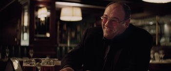 Movie still from “Killing Them Softly” (2012), directed by Andrew Dominik – A man sitting at a table with a drink in front of him; Close Up shot, Over the shoulder angle
