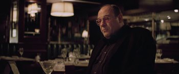 Movie still from “Killing Them Softly” (2012), directed by Andrew Dominik – A man sitting at a table in front of a glass of wine; Medium shot, Low angle