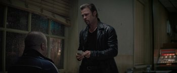 Movie still from “Killing Them Softly” (2012), directed by Andrew Dominik – A man in a leather jacket holding a cell phone; Medium shot, Over the shoulder angle