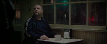 Movie still from “Killing Them Softly” (2012), directed by Andrew Dominik – A man sitting at a table in front of a window; Medium shot, Over the shoulder angle