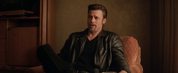 Movie still from “Killing Them Softly” (2012), directed by Andrew Dominik – A man sitting on a couch wearing a leather jacket; Medium shot, Over the shoulder angle