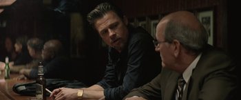 Movie still from “Killing Them Softly” (2012), directed by Andrew Dominik – A man sitting next to another man in a room; Medium shot, Over the shoulder angle