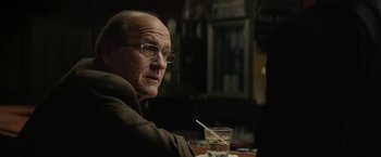 Movie still from “Killing Them Softly” (2012), directed by Andrew Dominik – An older man sitting at a table in front of a glass of water; Close Up shot, Over the shoulder angle