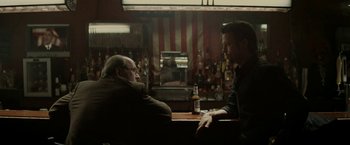 Movie still from “Killing Them Softly” (2012), directed by Andrew Dominik – Two men sitting at a table in front of a bottle of beer; Medium shot, Over the shoulder angle