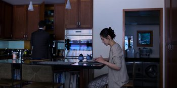 Movie still from “Kimi” (2022), directed by Steven Soderbergh – A woman sitting at a kitchen table using a laptop computer; Wide shot, Over the shoulder angle