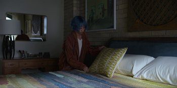 Movie still from “Kimi” (2022), directed by Steven Soderbergh – A woman with blue hair sitting on top of a bed next to pillows; Wide shot, High angle
