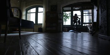 Movie still from “Kimi” (2022), directed by Steven Soderbergh – A person riding a bike on a wooden floor near a window; Extreme Wide shot, High angle