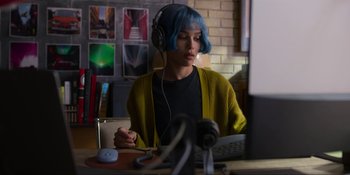 Movie still from “Kimi” (2022), directed by Steven Soderbergh – A person with blue hair is sitting at a desk; Medium shot, High angle