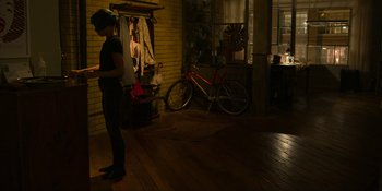 Movie still from “Kimi” (2022), directed by Steven Soderbergh – A person standing in a room with a bicycle; Wide shot, High angle