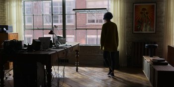 Movie still from “Kimi” (2022), directed by Steven Soderbergh – A woman standing in front of a window looking outside; Wide shot, High angle