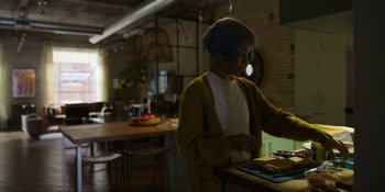 Movie still from “Kimi” (2022), directed by Steven Soderbergh – A woman standing in front of a table with food on it; Medium shot, Over the shoulder angle