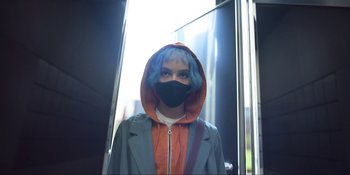 Movie still from “Kimi” (2022), directed by Steven Soderbergh – A person wearing a mask standing in front of a building; Close Up shot, Low angle