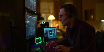 Movie still from “Kimi” (2022), directed by Steven Soderbergh – A man with a headset on sitting at a computer desk; Medium shot, Over the shoulder angle