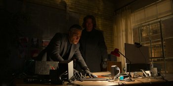 Movie still from “Kimi” (2022), directed by Steven Soderbergh – A man in a black suit and a man in a black suit and black gloves are at a computer desk; Medium shot, Low angle