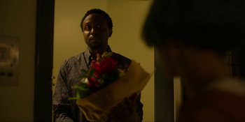 Movie still from “Kimi” (2022), directed by Steven Soderbergh – A man holding a bouquet of flowers in front of a mirror; Medium shot, Over the shoulder angle