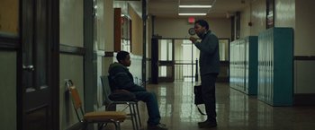 Movie still from “Kin” (2018), directed by Josh Baker – Two men are sitting in a hallway and one man is holding a microphone; Wide shot, Low angle