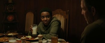 Movie still from “Kin” (2018), directed by Josh Baker – A man sitting at a table with a glass of milk; Medium shot, Over the shoulder angle