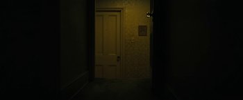 Movie still from “Kin” (2018), directed by Josh Baker – A door way leading to a dark room with a light shining on it; Wide shot, High angle