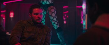 Movie still from “Kin” (2018), directed by Josh Baker – A man sitting in front of a woman in fishnet stockings; Medium shot, Over the shoulder angle