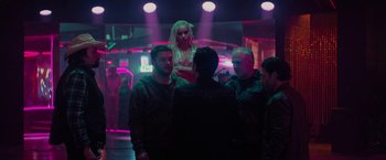 Movie still from “Kin” (2018), directed by Josh Baker – A group of men standing around a woman in a dark room; Wide shot, Over the shoulder angle
