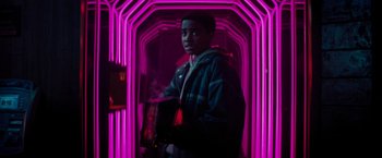 Movie still from “Kin” (2018), directed by Josh Baker – A young man standing in a neon tunnel holding a bag; Medium shot, Low angle