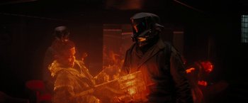 Movie still from “Kin” (2018), directed by Josh Baker – A man wearing a gas mask in front of a fire; Medium shot, Over the shoulder angle