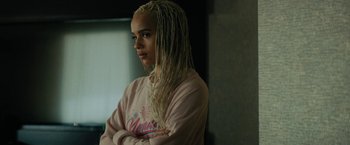 Movie still from “Kin” (2018), directed by Josh Baker – A woman with blonde dreadlocks standing with her arms crossed; Close Up shot, Over the shoulder angle
